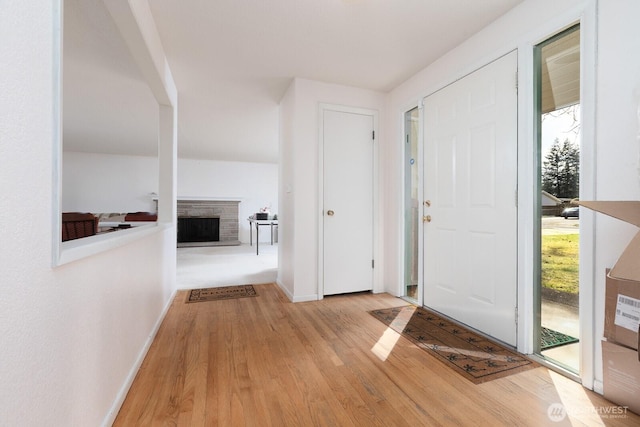 foyer featuring light wood-style flooring, baseboards, and a fireplace with raised hearth