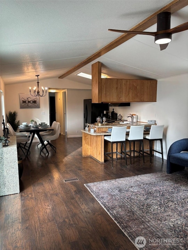 kitchen with dark wood-style floors, brown cabinetry, a peninsula, vaulted ceiling with beams, and a kitchen breakfast bar