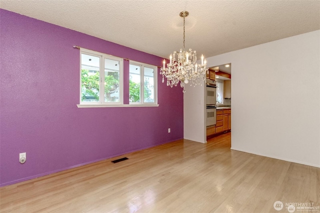 unfurnished dining area featuring an inviting chandelier, light wood-style flooring, visible vents, and a textured ceiling