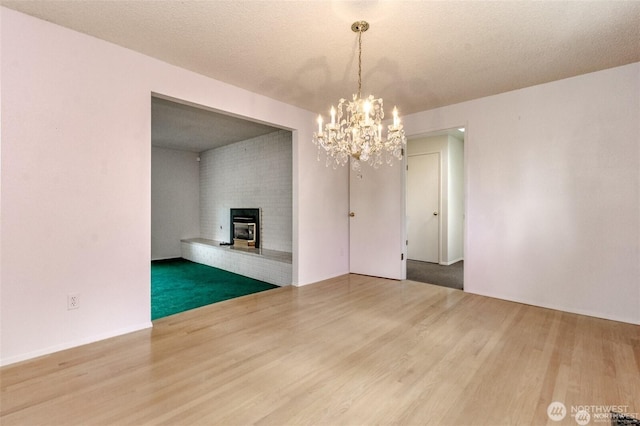 unfurnished dining area featuring a brick fireplace, a notable chandelier, a textured ceiling, and wood finished floors