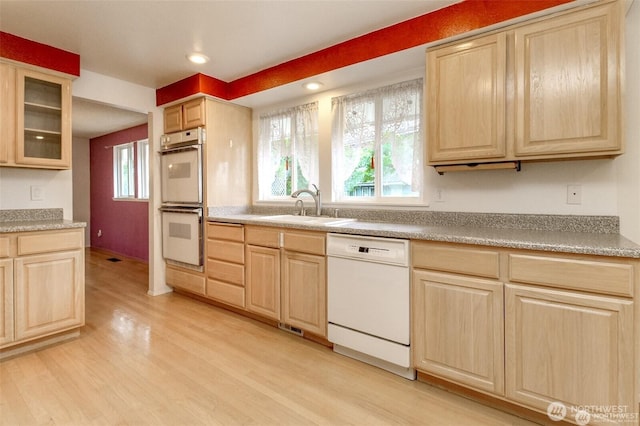 kitchen featuring light brown cabinetry, white appliances, and a sink