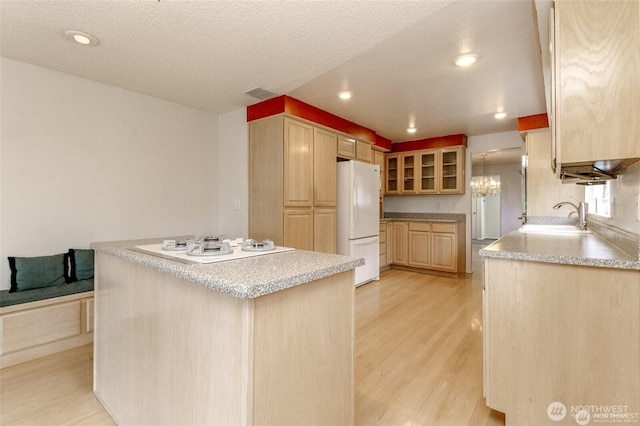 kitchen with glass insert cabinets, light brown cabinets, a sink, light wood-type flooring, and white appliances