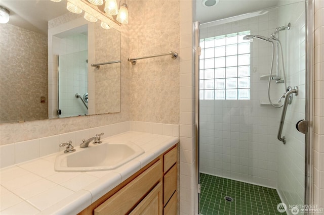 bathroom with wallpapered walls, a shower stall, and vanity