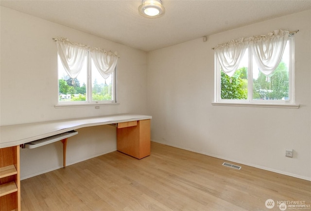 unfurnished office with light wood-style flooring, built in desk, visible vents, and baseboards