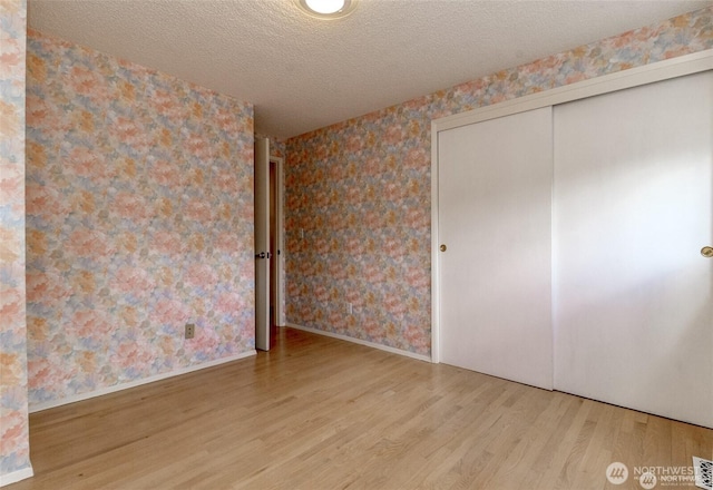 unfurnished bedroom with a textured ceiling, a closet, wood finished floors, and visible vents