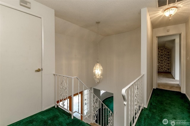 hall with visible vents, carpet floors, a textured ceiling, and an upstairs landing