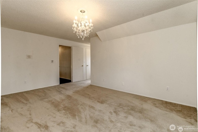 carpeted empty room featuring a textured ceiling and a notable chandelier