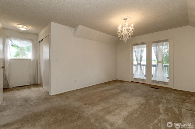 unfurnished room featuring visible vents, lofted ceiling, carpet, a textured ceiling, and a chandelier