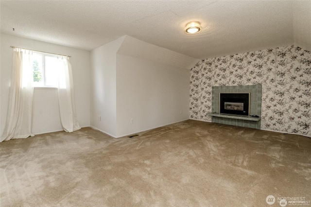 unfurnished living room featuring lofted ceiling, a tiled fireplace, visible vents, and wallpapered walls