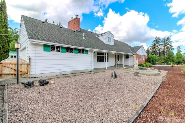 rear view of house featuring a shingled roof, a chimney, and fence