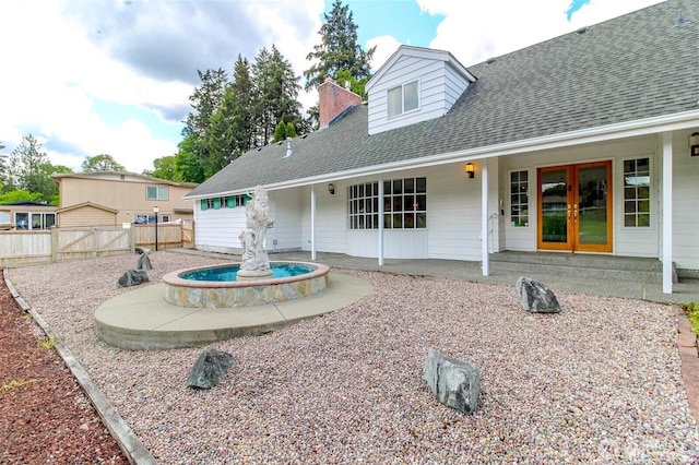 rear view of house with a chimney, roof with shingles, fence, french doors, and a patio area