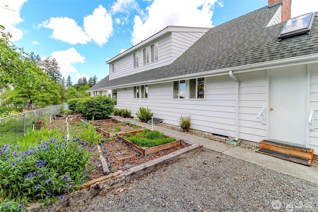 view of property exterior featuring entry steps, fence, a vegetable garden, and roof with shingles