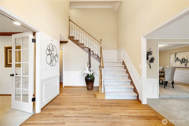 stairs with crown molding, a decorative wall, wood finished floors, and wainscoting