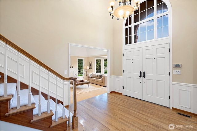 foyer entrance with visible vents, stairway, wainscoting, light wood finished floors, and a chandelier