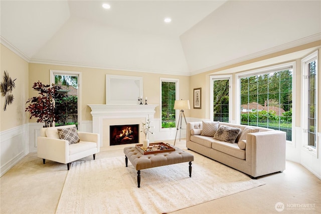 living area with a decorative wall, a lit fireplace, crown molding, wainscoting, and lofted ceiling