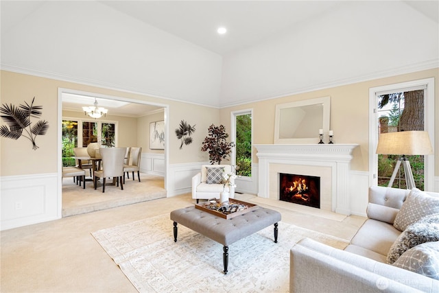 carpeted living area featuring a wealth of natural light, a wainscoted wall, a fireplace with flush hearth, and an inviting chandelier