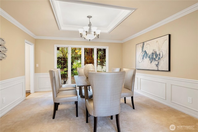 dining room with a decorative wall, a wainscoted wall, light colored carpet, a notable chandelier, and a raised ceiling