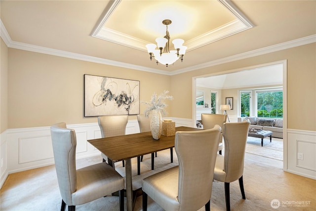 dining room featuring ornamental molding, wainscoting, a raised ceiling, a notable chandelier, and light colored carpet