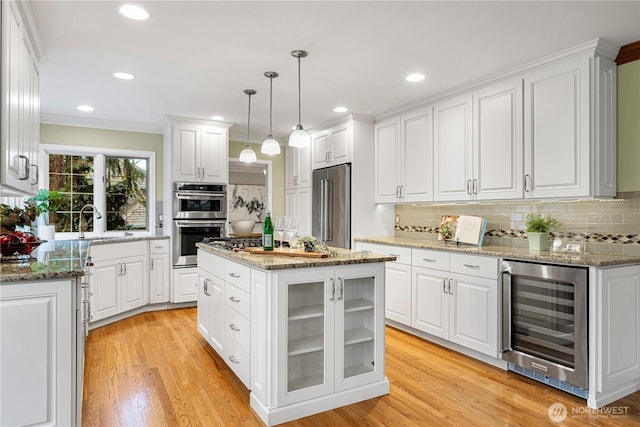 kitchen featuring beverage cooler, light wood-type flooring, appliances with stainless steel finishes, white cabinetry, and a sink