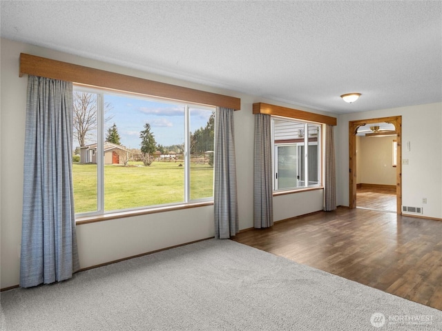 carpeted spare room featuring visible vents, a textured ceiling, baseboards, and wood finished floors