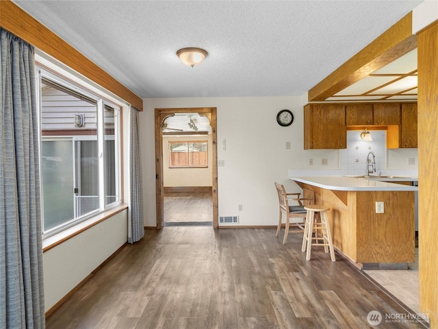 kitchen featuring wood finished floors, visible vents, a sink, light countertops, and a kitchen bar