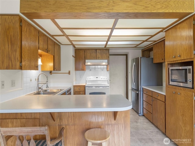 kitchen featuring a sink, under cabinet range hood, stainless steel appliances, a peninsula, and light countertops