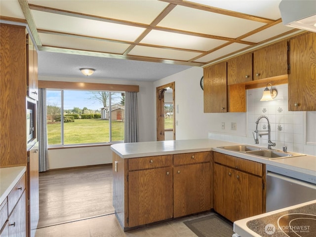 kitchen with brown cabinets, a peninsula, light countertops, and a sink