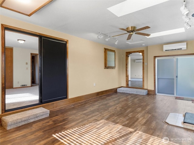 interior space with visible vents, ceiling fan, a skylight, wood finished floors, and a wall mounted AC