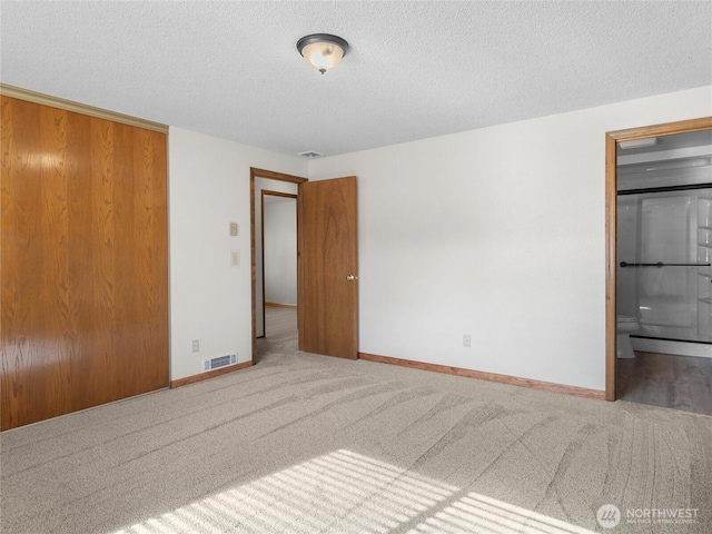 unfurnished bedroom featuring baseboards, visible vents, carpet floors, a textured ceiling, and connected bathroom