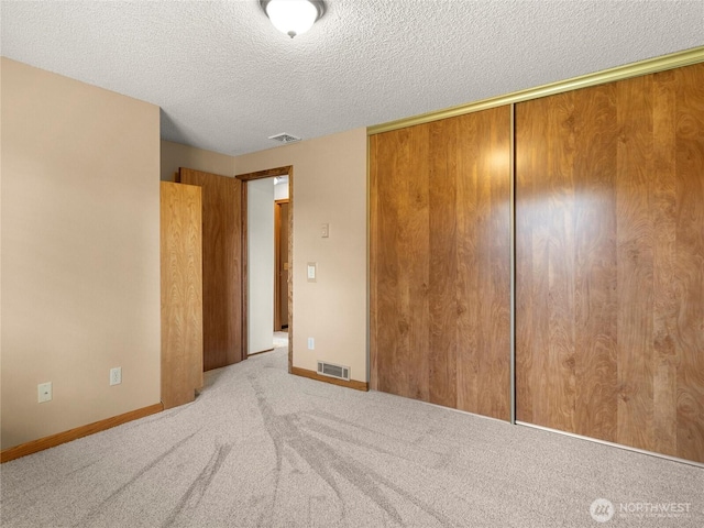 unfurnished bedroom featuring visible vents, carpet floors, a textured ceiling, and a closet