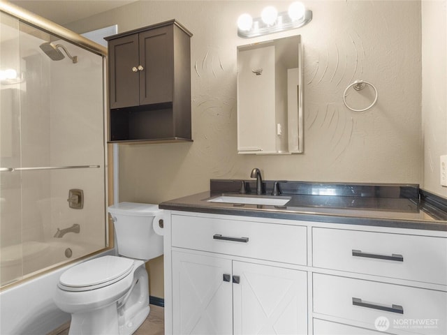 full bath with toilet, vanity, a textured wall, and shower / bath combination with glass door