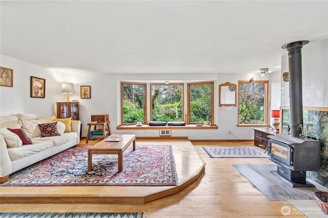 living room featuring visible vents, wood finished floors, a wood stove, and baseboards