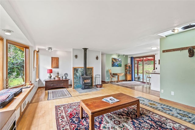 living room with visible vents, light wood-style floors, a wood stove, track lighting, and baseboards