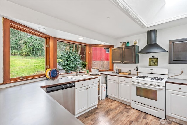 kitchen with white gas stove, white cabinetry, a sink, dishwasher, and wall chimney exhaust hood