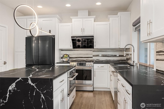 kitchen featuring stainless steel appliances, wood finished floors, a sink, white cabinets, and backsplash