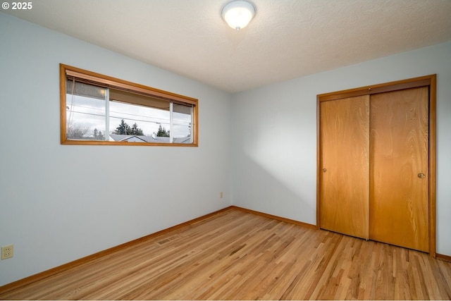 unfurnished bedroom featuring baseboards, a closet, light wood finished floors, and a textured ceiling