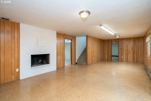 unfurnished living room with speckled floor, wooden walls, a brick fireplace, and stairway