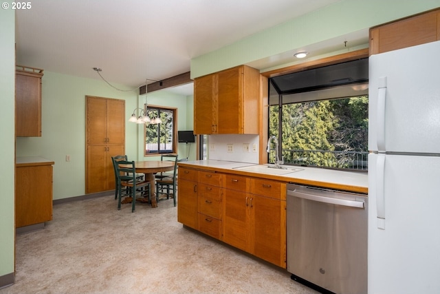 kitchen with a sink, freestanding refrigerator, brown cabinetry, light countertops, and dishwasher