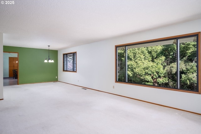 unfurnished room with baseboards, a notable chandelier, carpet flooring, and a textured ceiling