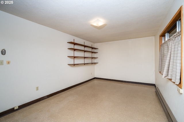 spare room featuring a textured ceiling, baseboards, speckled floor, and a baseboard radiator
