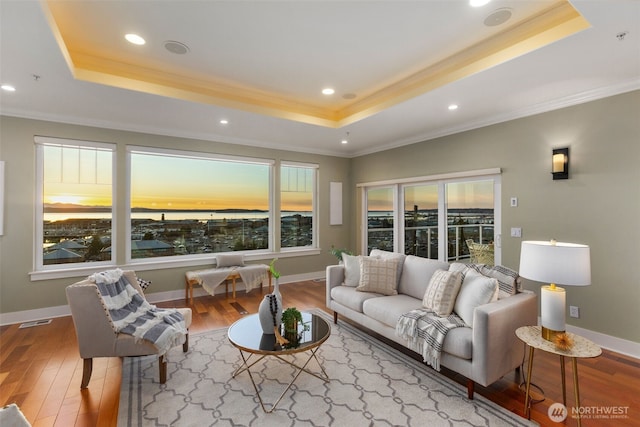 living area with a raised ceiling, wood finished floors, baseboards, and ornamental molding