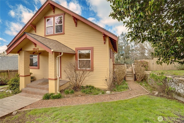 bungalow-style home with brick siding, roof with shingles, a front lawn, and fence