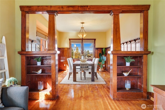 dining room with wood finished floors, wainscoting, and ornate columns