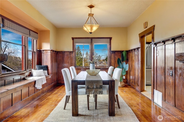 dining area with a wainscoted wall, light wood-style flooring, and visible vents