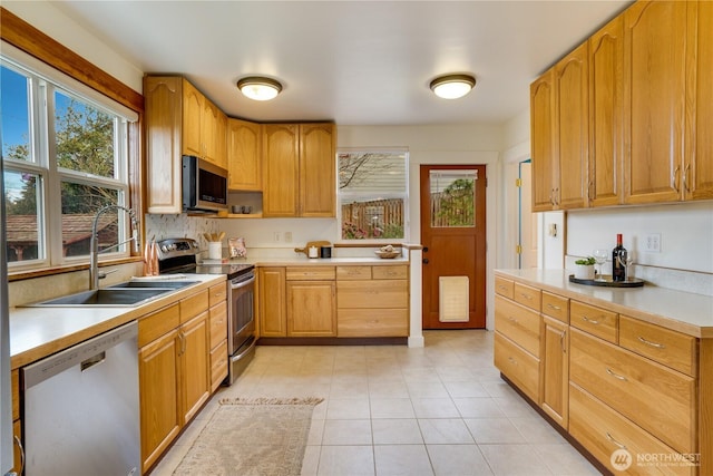 kitchen with light countertops, light tile patterned flooring, appliances with stainless steel finishes, and a sink