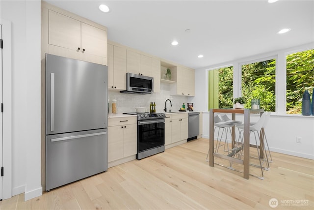 kitchen featuring light countertops, light wood-style flooring, decorative backsplash, appliances with stainless steel finishes, and a sink