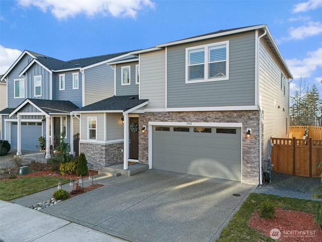 view of front facade featuring stone siding, an attached garage, concrete driveway, and fence