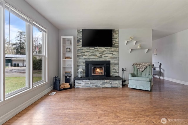 living room with a stone fireplace, baseboards, visible vents, and wood finished floors