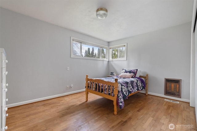 bedroom featuring hardwood / wood-style flooring, heating unit, baseboards, and visible vents