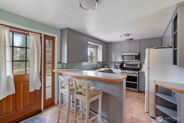 kitchen with a breakfast bar area, a peninsula, open shelves, gray cabinets, and appliances with stainless steel finishes